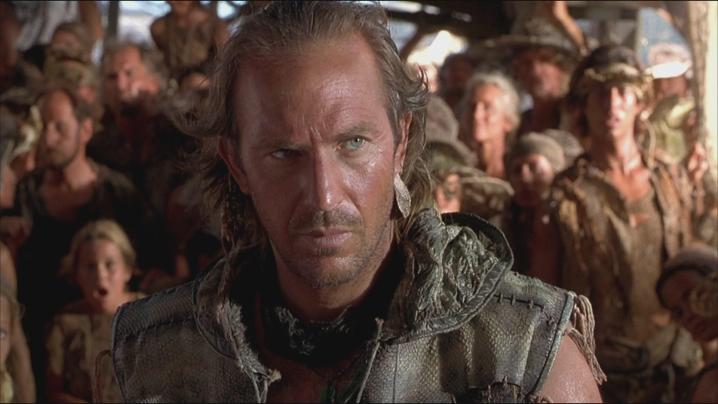 Kevin Costner stands in front of a group of people in Waterworld.